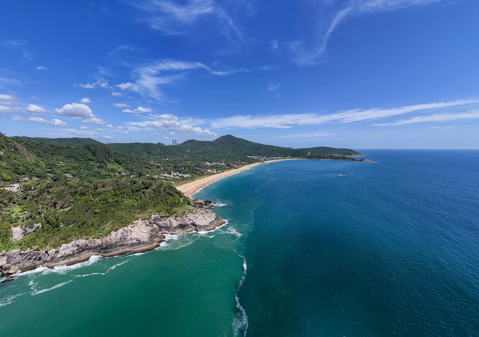 A Praia do Estaleiro vista do alto: o costão de pedra, a faixa de areia, a mata e, ao fundo, os morros da Interpraias